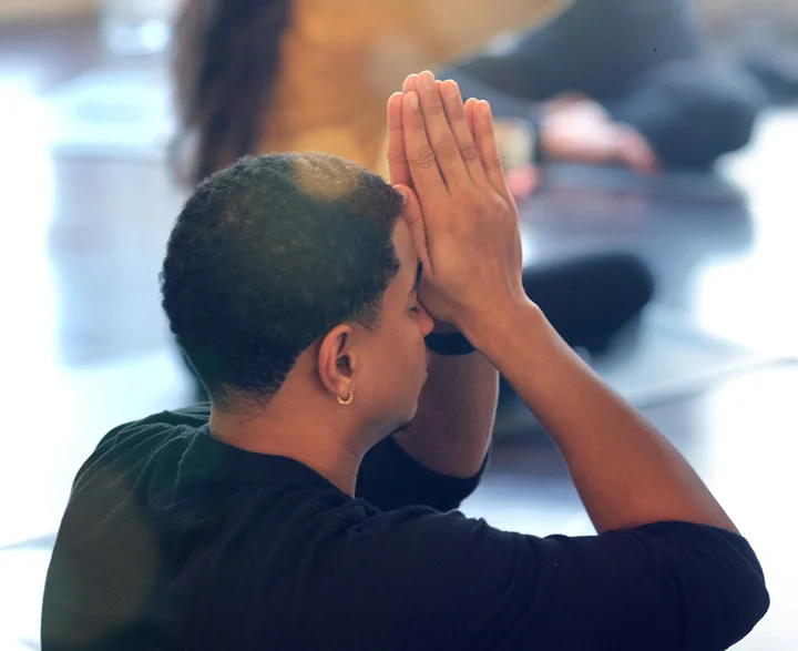 Male seated with hands in prayer, resting gently against the head.